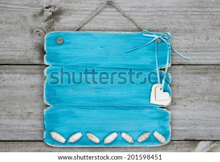 Blank antique teal blue wood sign with seashells and hearts hanging on rustic wooden background; beach sign with painted copy space