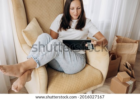 Woman sitting in a chair, holding credit bank card and using tablet for online shopping at home. Selective focus