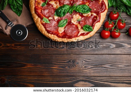 Pita pizza with pepperoni, cheese, basil and tomatoes on wooden table, flat lay. Space for text