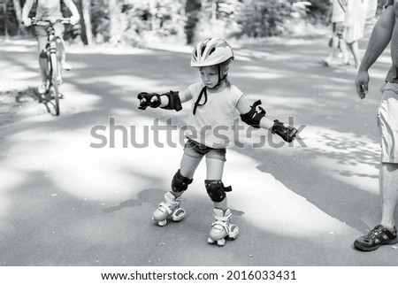 little girl is rollerblading in the park. baby in protective sportswear. black and white photo