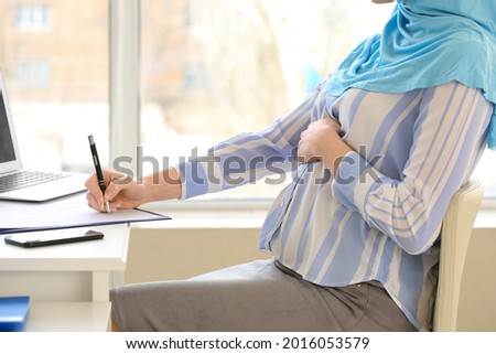Pregnant Muslim woman working in office
