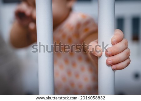 Cute little hand of a 6 month old baby holding a white crib frame.