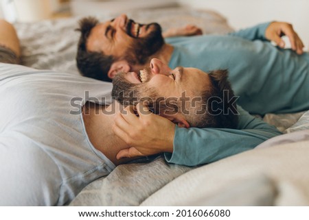 Happy gay couple lying down on the bed at home, hugging and flirting. Royalty-Free Stock Photo #2016066080