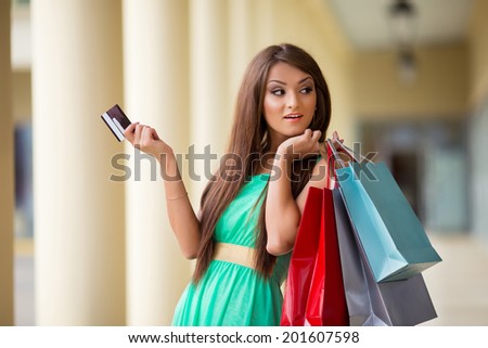 stunning and very beautiful woman in dress with long brown hair holding card and colored shopping bags