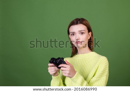 Young woman with perfect natural makeup brown big lips in casual sweater on green background with joystick playing video games