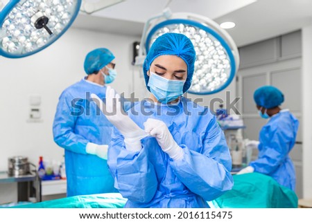 Portrait of female woman nurse surgeon OR staff member dressed in surgical scrubs gown mask and hair net in hospital operating room theater making eye contact smiling pleased happy looking at camera Royalty-Free Stock Photo #2016115475
