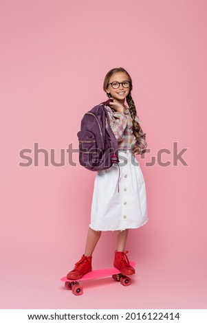 Smiling schoolchild riding penny board on pink background Royalty-Free Stock Photo #2016122414
