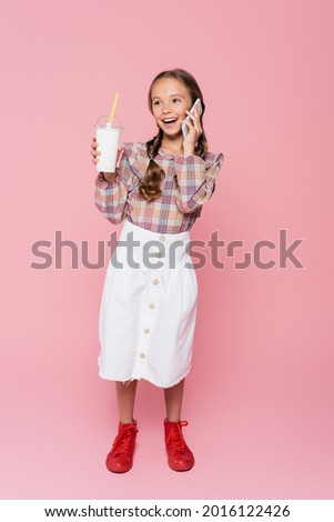 Kid with milkshake talking on smartphone on pink background