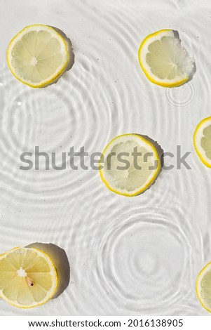 Abstract water texture with wet lemon slices, surface with drops, rings and ripple.
Flat lay, top view, skin care or food background with copy space