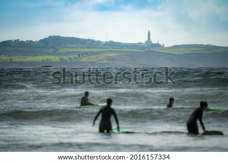People walking with surfboards and surfing, in the city of Somo in the province of Santander, Spain, near large cliffs and virgin beaches