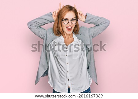 Young caucasian woman wearing business style and glasses posing funny and crazy with fingers on head as bunny ears, smiling cheerful 
