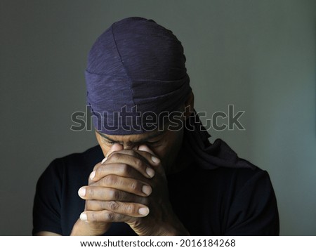 man praying to god Caribbean man praying with hands together on grey background stock photo