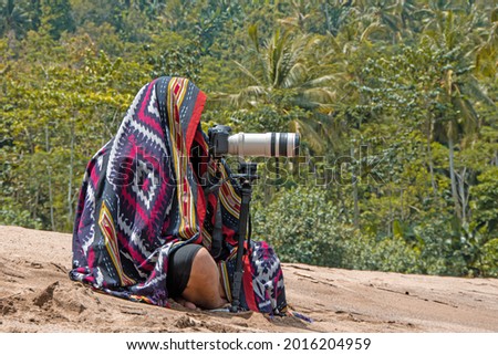 The photographer hid behind the colored cloth of camouflage photography, waiting with his camera gear to take pictures of birds and animals. Malang - August 30 - East Java - Indonesia