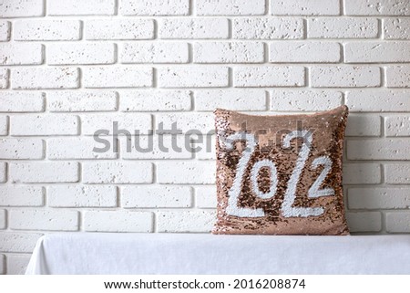 Golden pillow  with paillettes with inscription 2022. Pillow with sequins on brick wall background. Place for text