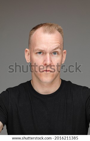portrait of caucasian man in black t-shirt looks to the camera with a doubt isolated on grey background
