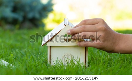 The child collects a mock-up of a wooden house on the green grass. Close-up of hands. Family values. A house built by your own hands. Place for your text.