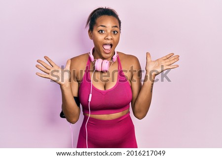 Young african american girl wearing gym clothes and using headphones celebrating crazy and amazed for success with arms raised and open eyes screaming excited. winner concept 