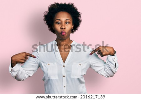 African american woman with afro hair pointing with fingers to herself making fish face with mouth and squinting eyes, crazy and comical. 