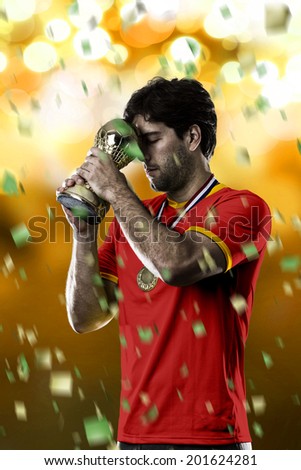 belgian soccer player, celebrating the championship with a trophy in his hand. On a yellow lights background.