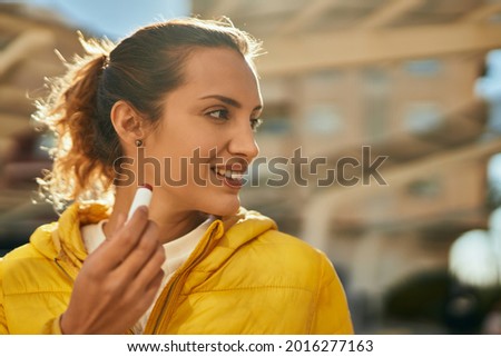 Young hispanic girl smiling happy using lipstick at the city.