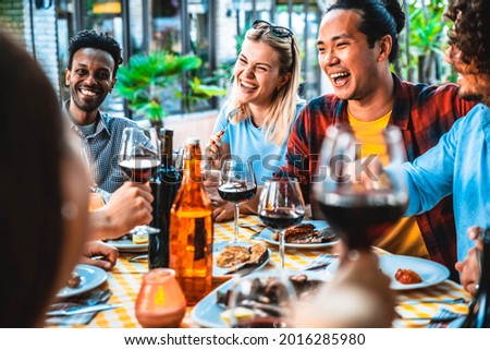 Group of friends having fun at bbq dinner outdoor in garden restaurant - Multiracial people eating food at barbecue backyard home party - Friendship, youth and party concept