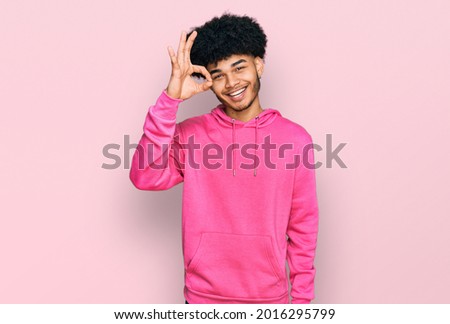 Young african american man with afro hair wearing casual pink sweatshirt smiling positive doing ok sign with hand and fingers. successful expression. 