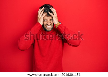 Handsome man with beard wearing casual red sweater suffering from headache desperate and stressed because pain and migraine. hands on head. 