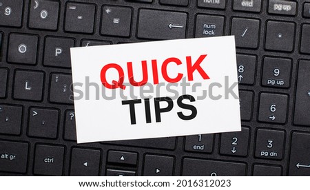 On a black computer keyboard there is a white card with the text QUICK TIPS. View from above
