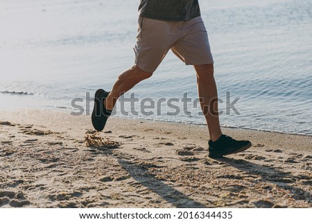 Cropped up photo legs shot young sporty sportsman man 20s wear sports clothes black shorts shorts run warm up training at sunrise sun dawn over sea beach outdoor on pier seaside in summer day morning