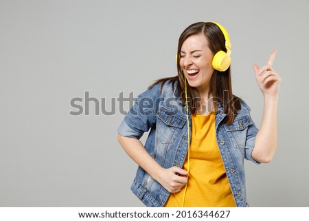 Young fun happy caucasian woman 20s wear casual trendy denim jacket yellow t-shirt headphones point index finger up dancing isolated on grey color background studio portrait. People lifestyle concept.