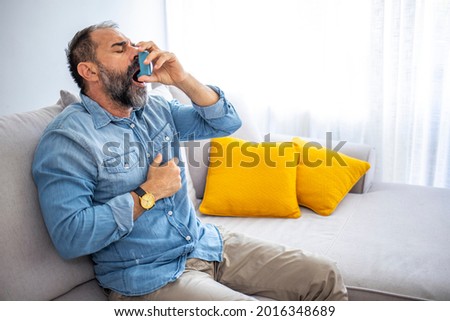 Man using asthma inhaler. Man using asthma inhaler for relief an attack at home for preventing attack. Man using medical inhaler to prevent and treat wheezing and shortness of breath caused by allergy