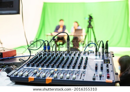 2 people acting as hosts for a live program or make an online stream via internet on the green scene by the sound mixer that is currently broadcasting or recording the show.