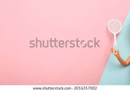 Doll hand holding tennis racket on blue-pink pastel background. Minmalism, concept art. Copy space