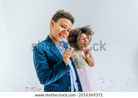 Happy girl and boy having fun time on the party with paper decor clown nose and glasses on white background. Selective focus on the boy's face.