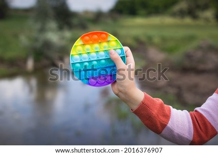 A little cute girl is holding a bright, colorful anti-stress toy pop it.