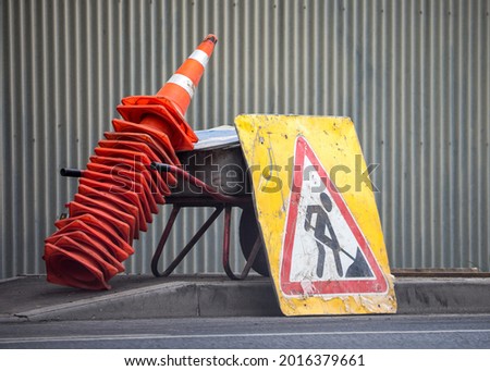 Under construction board sign, traffic cones and a wheel barrow