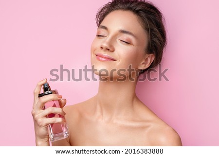 Woman with bottle of perfume. Photo of woman with perfect makeup on pink background. Beauty concept