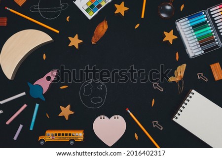 Rocket, moon, stars, school bus and supplies on a black background with space for text in the middle, close-up top view.