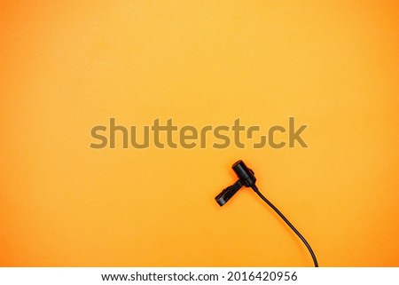 Lavalier microphone on an orange background.