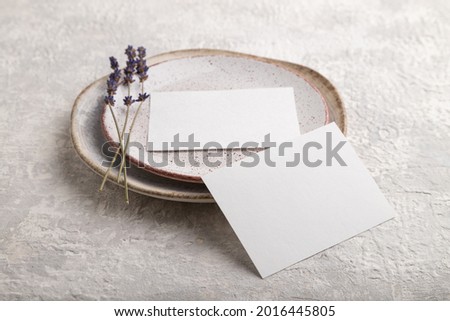 White paper invitation card, mockup with lavender on ceramic plate and gray concrete background. Blank, side view, still life, copy space.