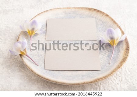 Gray paper invitation card, mockup with crocus flowers on ceramic plate and gray concrete background. Blank, flat lay, top view, still life, copy space, wedding invitation.