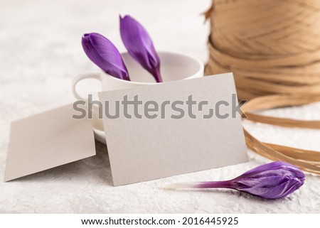 Gray paper invitation card, mockup with purple crocus snowdrop flowers on gray concrete background. Blank, side view, still life, copy space, wedding invitation.