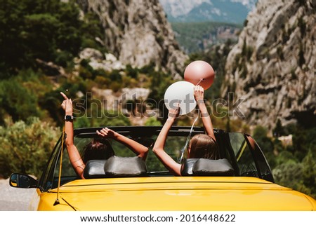 Two young woman with hands up enjoying vacation driving picturesque mountain view road