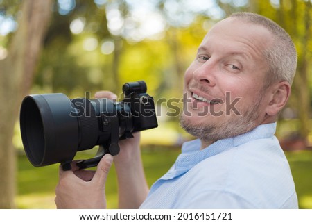 adult man makes a photo on a camera with a large lens. In the park on a sunny day in summer.