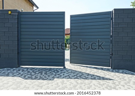 one open black metal gate and part of a brick wall of a fence on the street on a gray sidewalk Royalty-Free Stock Photo #2016452378