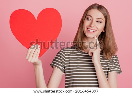 Portrait of cunning girlish flirty lady presenting red heart symbol on pink background