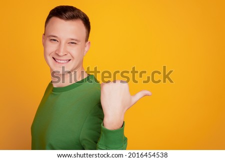 Portrait of cheerful handsome guy toothy smile indicate thumb empty space on yellow background