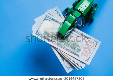 A pack of 100 dollar bills in mouth of tyrannosaur green kid toy isolated on blue background. Copy space.