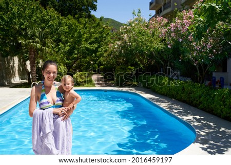 Smiling mom holds a little girl in her arms while standing by the pool