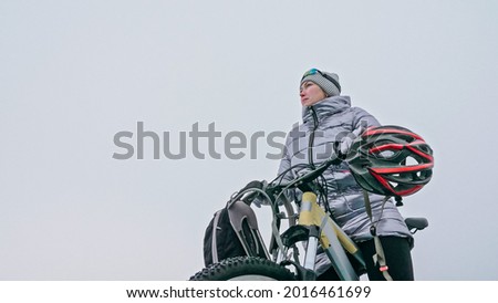 Woman stands near her bike on ice. The girl cyclist stopped to r